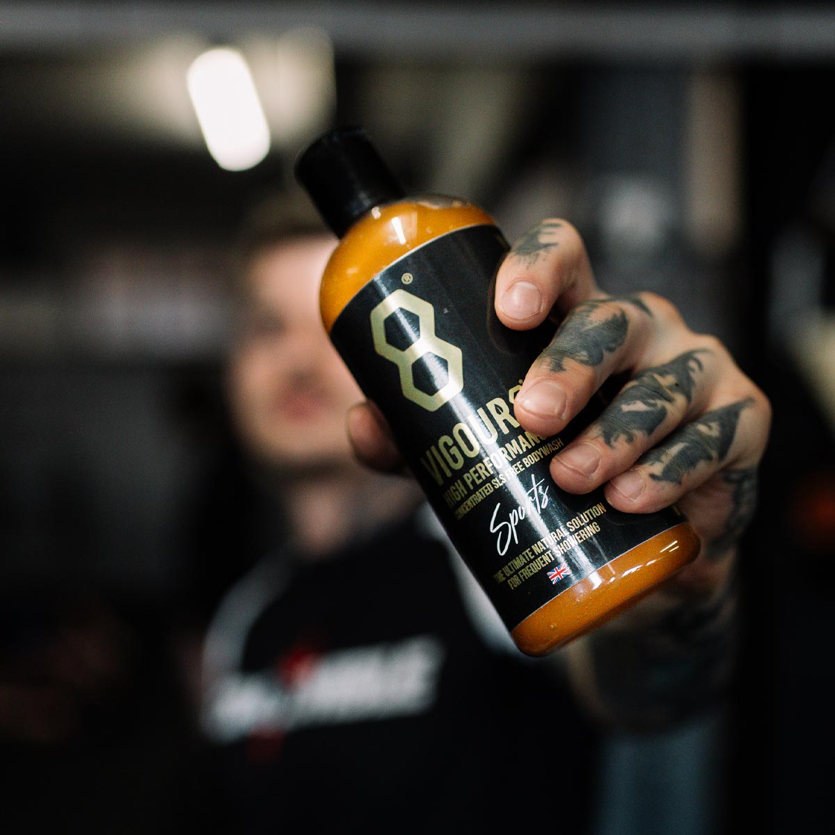 Hand holding a bottle of Vigour8 bodywash with a blurred background